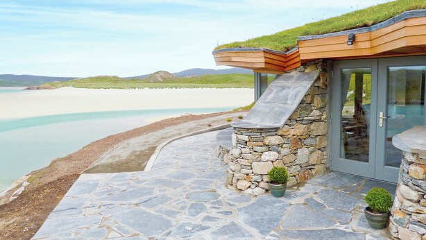 A stone building with a glass door, a stone pathway, and a grassy roof.
