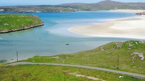A coastal landscape with a sandy beach, calm waters, and rolling hills in the background.