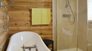 A bathroom with a wooden wall, a white bathtub, a shower enclosure, and a towel rack with a yellow towel. - 1 bedroom accommodation in South Carlton, near Lincoln (South Carlton, near Lincoln)