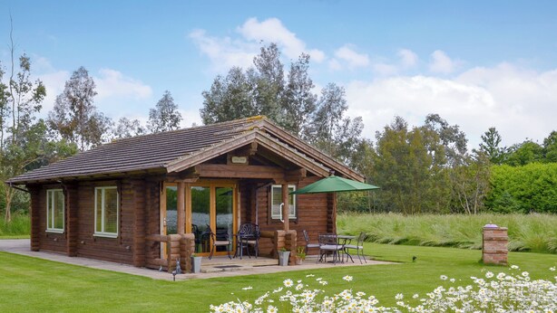 A rustic log cabin with a patio, outdoor seating, and a lawn with daisies. - 1 bedroom accommodation in South Carlton, near Lincoln (South Carlton, near Lincoln)