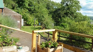 A wooden deck with a railing, a small building with a green roof, and a lush green landscape in the background. - 2 bedroom accommodation in Graigfechan, near Ruthin (Graigfechan, near Ruthin)