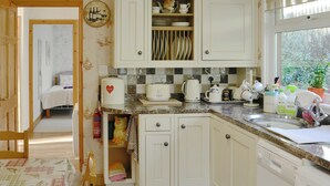 A kitchen with white cabinets, a countertop with various appliances, and a window with a view of greenery. - 2 bedroom accommodation in Graigfechan, near Ruthin (Graigfechan, near Ruthin)