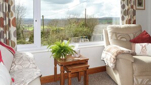 A cozy room with a large window, a wooden table with a plant, a cushioned chair, and a view of the countryside. - 2 bedroom accommodation in Graigfechan, near Ruthin (Graigfechan, near Ruthin)