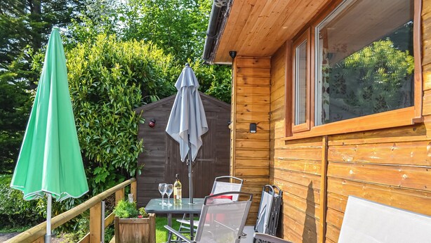A wooden deck with outdoor furniture, a table with wine glasses, and a green umbrella. - 2 bedroom accommodation in Graigfechan, near Ruthin (Graigfechan, near Ruthin)