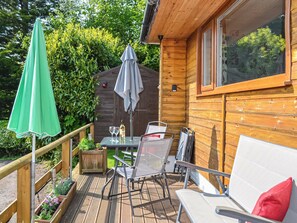 Una terraza de madera con mobiliario exterior, una mesa con copas de vino y un paraguas verde.