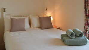 A neatly made bed with white and beige bedding, a bedside lamp, and a stack of green towels on the right side. - 2 bedroom accommodation in Alnwick (Alnwick)