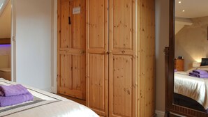 Une chambre avec une grande armoire en bois, un lit recouvert d’une couette blanche et agrémenté de serviettes violettes, et un miroir qui reflète la pièce.