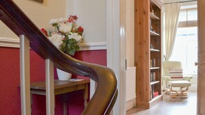 Un escalier avec une rampe, une bibliothèque en bois, une chaise et une fenêtre avec des rideaux.