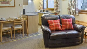 A compact living space with a dining area, a kitchenette, and a leather armchair with plaid cushions.
