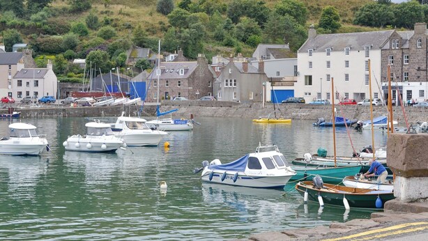 A harbor with boats docked, a stone quay, and buildings in the background.