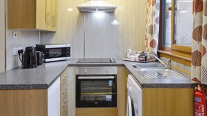 A compact kitchen with wooden cabinets, a microwave, a kettle, a dishwasher, and a washing machine.