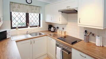 A modern kitchen with white cabinets, a stainless steel oven, a built-in microwave, and a window with a floral curtain.