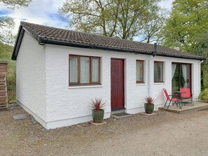 A single-story house with a tiled roof, a red door, and a small porch with a table and chairs.