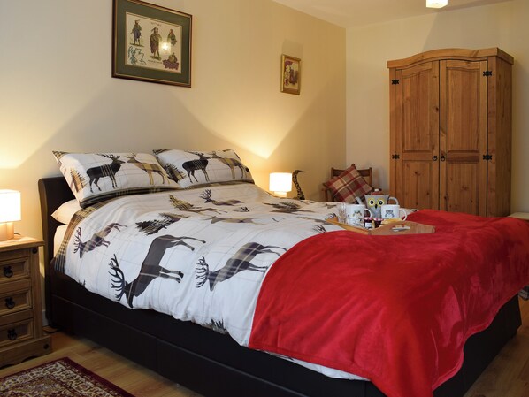 A bedroom with a bed featuring a moose print bedspread, a red throw blanket, a wooden wardrobe, and two wall-mounted lamps.