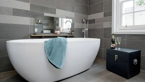 Un bagno moderno con una vasca freestanding, un asciugamano, una bottiglia di champagne e un piccolo mobiletto.