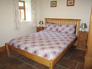 Un lit en bois avec une couvre-lit à motifs, deux tables de chevet avec des lampes, une fenêtre avec des rideaux et un sol carrelé.