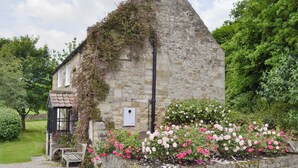 Een gebouw van steen met een schuin dak, omgeven door een grindpad en een bloembed met roze en witte bloemen.