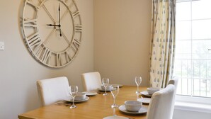 A dining room with a wooden table set for four, a large wall clock, and a window with curtains. - 3 bedroom accommodation in Edinburgh (Edinburgh)