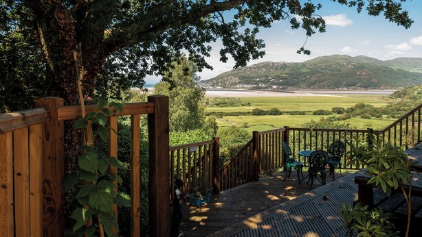 A wooden deck with a view of a coastal landscape, including a beach and hills. - 4 bedroom accommodation in Arthog, near Dolgellau (Arthog, near Dolgellau)