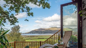 A deck with wicker furniture, a glass door, and a view of a valley and mountains. - 4 bedroom accommodation in Arthog, near Dolgellau (Arthog, near Dolgellau)