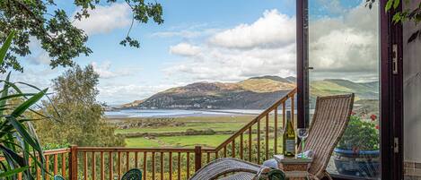 A deck with wicker furniture, a glass door, and a view of a valley and mountains.