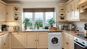 A kitchen with white cabinets, a built-in washing machine, a stove, and a window with a view of the outdoors. - 4 bedroom accommodation in Arthog, near Dolgellau (Arthog, near Dolgellau)
