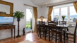 A dining area with a table set for four, surrounded by wooden chairs, a television on a wooden stand, and a potted plant. - 4 bedroom accommodation in Arthog, near Dolgellau (Arthog, near Dolgellau)