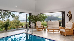 A pool area with a view of a lake and mountains, surrounded by wicker furniture and a large potted plant. - 4 bedroom accommodation in Arthog, near Dolgellau (Arthog, near Dolgellau)