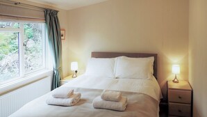 A neatly made bed with two towels, a bedside lamp, and a window with curtains.
