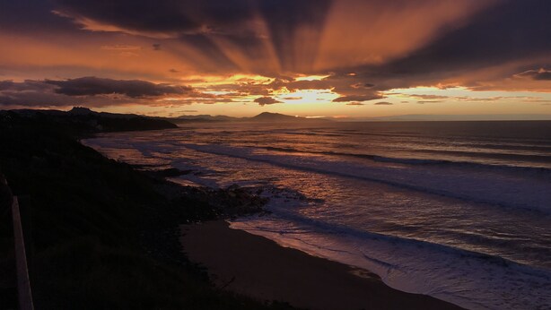 Una puesta de sol sobre una playa con olas y una lejana cadena montañosa.