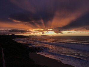 A sunset over a beach with waves and a distant mountain range.