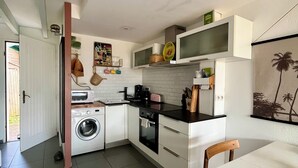 Cocina compacta equipada con lavadora, microondas y horno. Cuenta con un comedor con mesa y sillas.