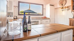 Une cuisine avec une grande fenêtre, deux bouteilles de vin et un verre transparent posé sur le comptoir.
