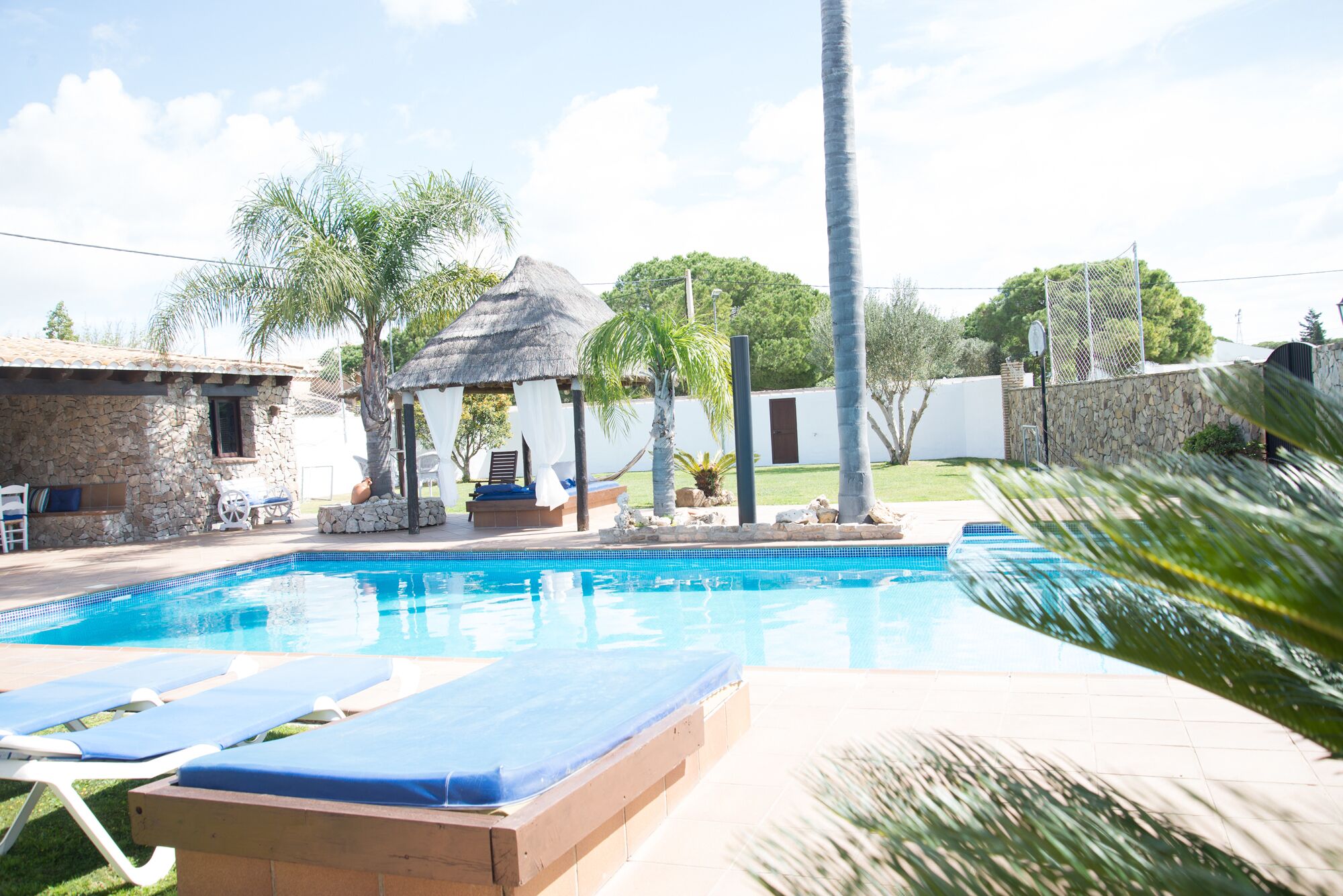 A swimming pool with lounge chairs, a gazebo, and stone walls.