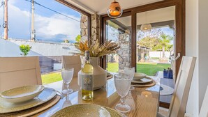 Une table à manger dressée avec des assiettes, des verres et une bouteille de vin, donnant sur un jardin et un mur de pierre.