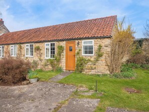 Une maison en pierre avec un toit en tuiles, une porte en bois et un petit jardin.