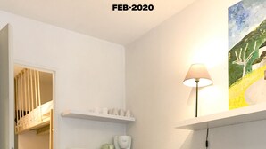 A cozy room with a bed, a sofa, a shelf with cups, a coffee maker, and a lamp.