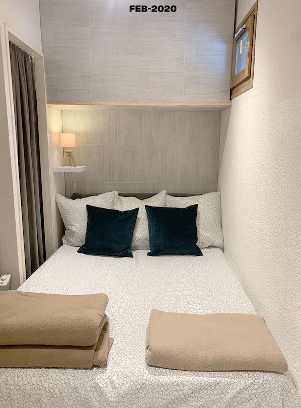 A small, neatly arranged bedroom with a bed, two pillows, a bedside lamp, and two towels.