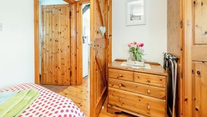 Ein Zimmer mit Holzboden, einem Bett, einer Kommode und einer Tür zu einem weiteren Raum.
