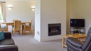 A living room with a fireplace, a TV, and a dining area with wicker furniture. - 2 bedroom accommodation in Upton, Didcot (Upton, Didcot)