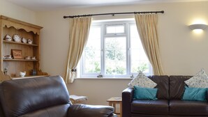 A living room with a leather armchair, a brown sofa with teal cushions, a wooden shelf with decorative items, and a window with curtains. - 2 bedroom accommodation in Upton, Didcot (Upton, Didcot)
