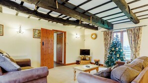 A cozy living room with leather sofas, a wooden ceiling, a television, and a decorated Christmas tree. - Timbers Barn - E3863 (Runcton Holme)