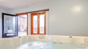 A spa room with a hot tub, a window with a view of a building, and a sign indicating the spa's operating hours. - Timbers Barn - E3863 (Runcton Holme)