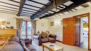 A cozy living room with a sofa, a coffee table, and a wooden door leading to a laundry area. - Timbers Barn - E3863 (Runcton Holme)