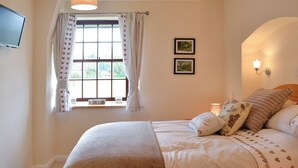 A bedroom with a bed, a window with curtains, a wall-mounted TV, framed pictures, and a bedside lamp. - Bridge House - UKC1340 (Heasley Mill, near South Molton)