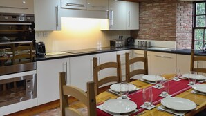 A modern kitchen with white cabinets, a brick wall, and a dining area set for four with a red table runner. - Bridge House - UKC1340 (Heasley Mill, near South Molton)
