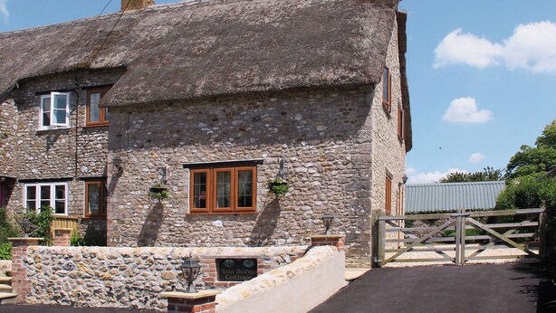 A stone cottage with a thatched roof, a wooden gate, and a sign indicating 'Two Bridges Cottage'. - 2 bedroom accommodation in Bridge, near Chard (Bridge, near Chard)