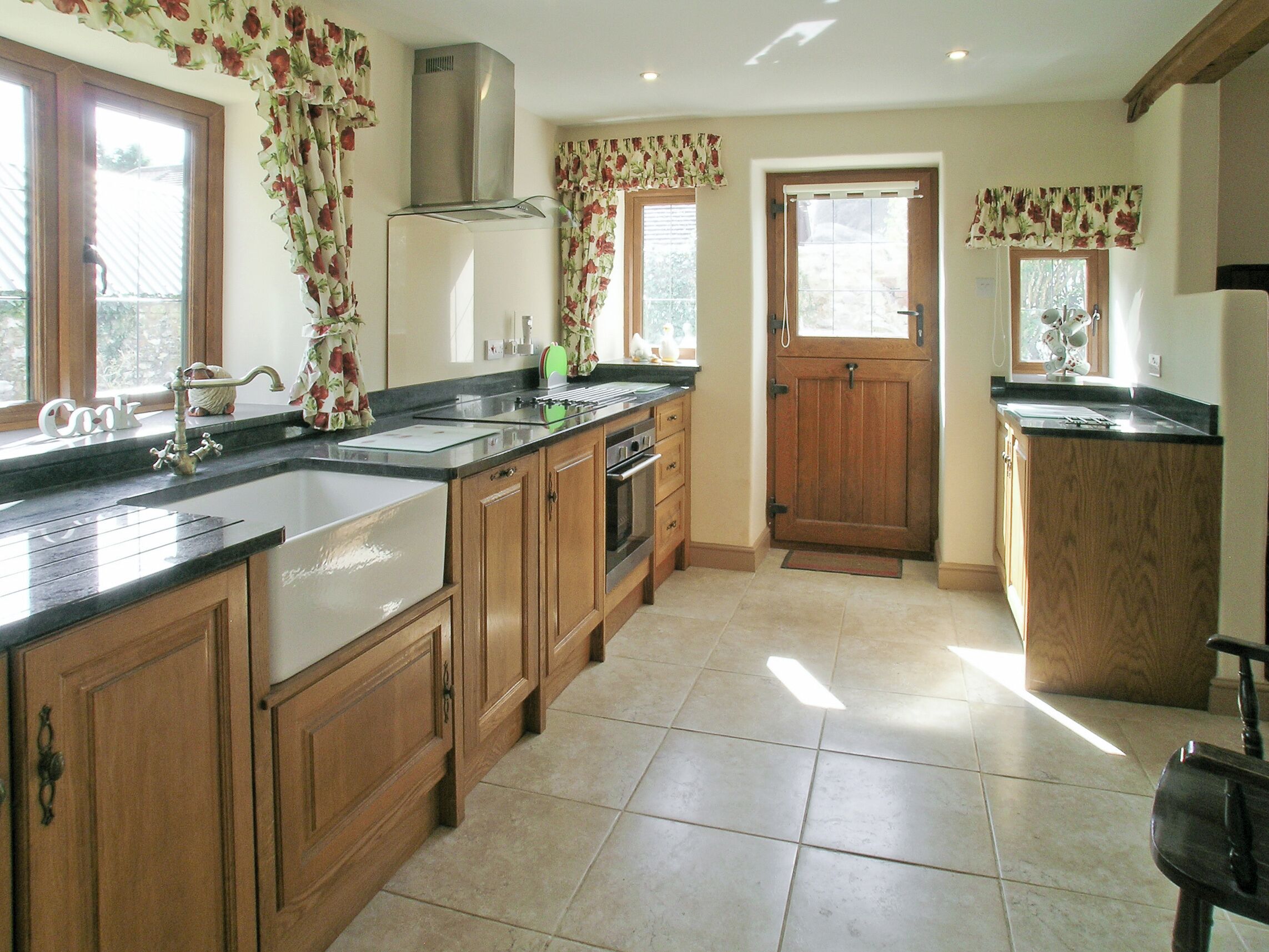 A kitchen with wooden cabinets, a stainless steel range hood, a double sink, and a wooden door.
