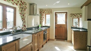 A kitchen with wooden cabinets, a stainless steel range hood, a double sink, and a wooden door. - 2 bedroom accommodation in Bridge, near Chard (Bridge, near Chard)