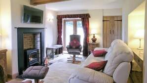 A cozy living room with a fireplace, a sofa, a chair, and a table. - 2 bedroom accommodation in Bridge, near Chard (Bridge, near Chard)